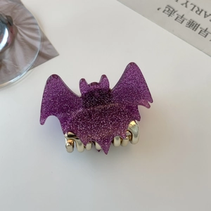 Detailed close-up of a purple glitter bat-shaped hair claw clip with golden metal teeth