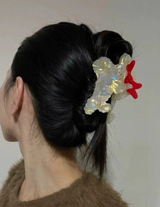 Detail view of the iridescent white hair claw clip with a red bow on dark hair