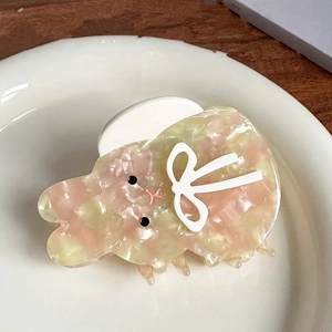 Détail d'une pince à cheveux lapin en acétate rose avec noeud sur une assiette en céramique
