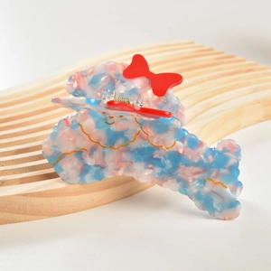 Detailed side view of a cute poodle hair claw clip with a red bow on a wooden plate