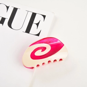 Close-up of pink and white acetate claw clip with spiral texture on a fashion magazine