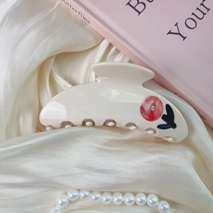 Detail of a creamy white acetate hair claw with red floral patterns and tiny rhinestones