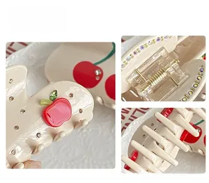 Detail view of beige hair claw clip with red cherry patterns and sparkling rhinestones