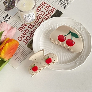 Elegant set of cream acetate hair claws with cherry patterns and rhinestones on a plate