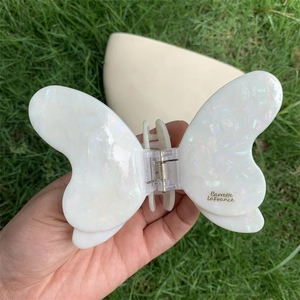 Iridescent butterfly hair claw clip in pearlescent acetate held against a green lawn
