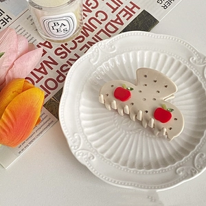 Detail of a creamy hair claw clip with red apple motifs and rhinestones on a porcelain plate
