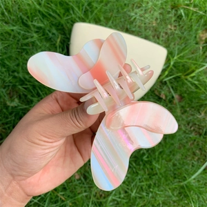 Detail of large butterfly hair claw clip with pink pearlescent gradient finish on grass