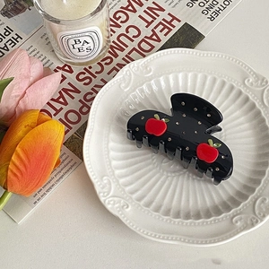Detail of black hair claw clip with red apple decoration and rhinestones on white plate