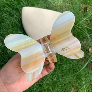 Detailed view of large iridescent acetate butterfly hair claw clip held on green grass