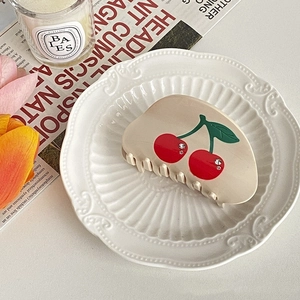 Detail view of cream hair claw with cherry print and rhinestone accents on porcelain plate