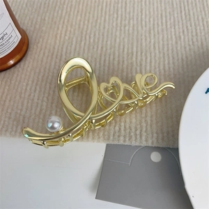 Detail der goldenen 'Love' Haarspange mit weißer Perle auf beigem Strickhintergrund