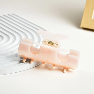 Detail of a creamy pink acetate hair claw clip with golden metal spring for daily use