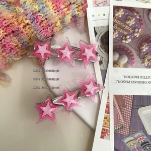 Gros plan de barrettes étoiles roses pailletées sur un fond de magazine esthétique