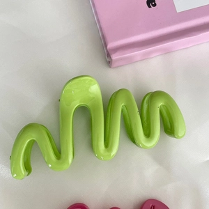 Glossy grass green wavy hair claw clip for women on pink book and white background