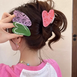 Acrylic heart hair claw clips in purple, green, and red worn on a hair bun