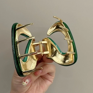 Detail of a large gold metal hair claw clip with green marble resin held in hand
