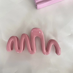 Close-up of a large wavy pink hair claw clip with glossy finish on soft white fabric