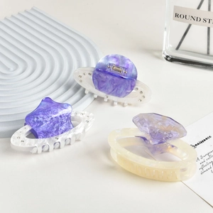 Close-up of three acetate hair claws in star, planet, and diamond shapes with rhinestones