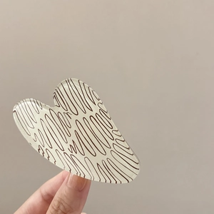 Detail view of a cream heart hair claw clip with brown wavy patterns held in hand