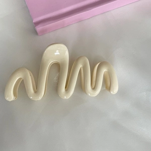 Detail showing the creamy white wavy hair claw clip with a glossy finish and smooth S-shape