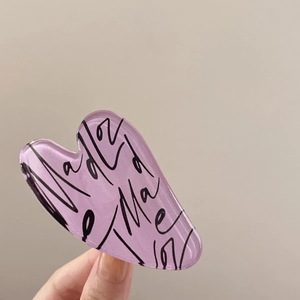Close-up of a purple heart-shaped acrylic hair claw clip with black script typography