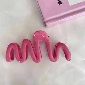 Detail of a large pink wave hair claw clip with a glossy finish on white fabric