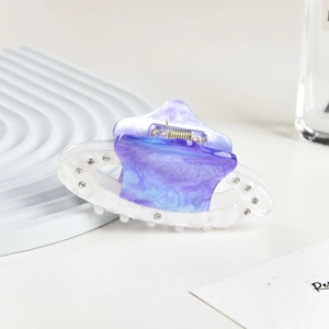 Macro detail of purple marble acetate hair claw clip with rhinestones on a white tray