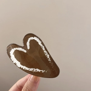 Detail showing deep brown heart-shaped hair claw with white minimalist line art design