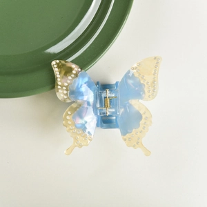 Detail of blue acetate butterfly hair claw clip with pearl embellishments on a ceramic tray