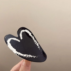 Macro shot of polished black heart hair claw clip with minimalist white heart outlines