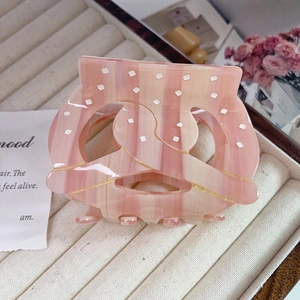 Close-up of pink marble acetate hair claw with white polka dots and gold glitter stripes