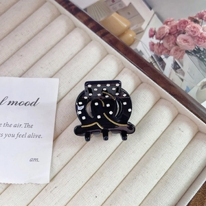 Detail of black acetate hair claw with white polka dots and gold wave lines on cream tray