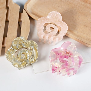Three acetate hollow flower hair claws in pastel pink and champagne on a wood tray