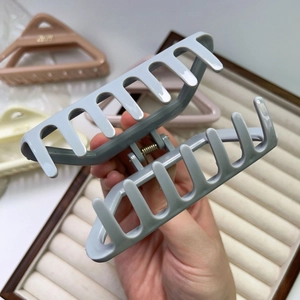 Detail showing hand holding a matte grey-blue hollow triangle hair claw clip with strong spring