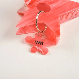 Détail macro d'une pince à cheveux étoile rose en acétate avec un petit pendentif fleur