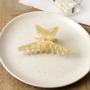 Détail d'une pince à cheveux papillon avec lettre B dorée sur surface crème marbrée