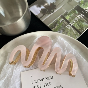 Détail de la pince à cheveux en acétate rose avec dents en métal doré sur assiette