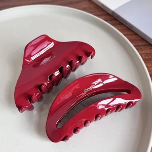 Detailed view of two dark red glossy acetate hair claws on a ceramic plate