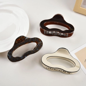 Three acetate hair claws in tortoise shell and cream colors on a beige desk