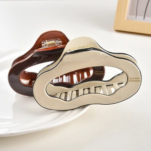 Detailed view of glossy cream and amber acetate hair claws with wave design and gold text
