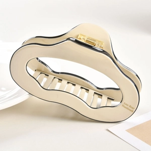 Detail view of large cream acetate hair claw clip with black trim and gold metal spring