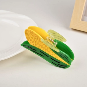Close-up of corn-shaped acetate hair claw clip with golden metal spring and green leaf detail
