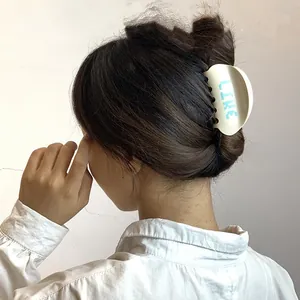 Dettaglio pinza per capelli color crema con scritta LIKE blu indossata da una modella