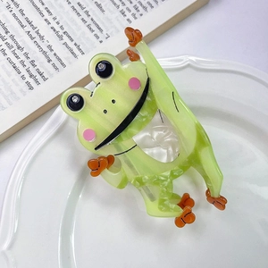 Vue détaillée d'une pince à cheveux grenouille en acétate vert sur une assiette blanche