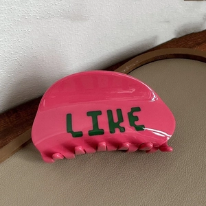Dettaglio della molletta per capelli rosa in acetato con scritta LIKE verde lucida