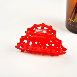 Detail of red acrylic spiderweb hair claw clip with golden metal spring and glossy finish