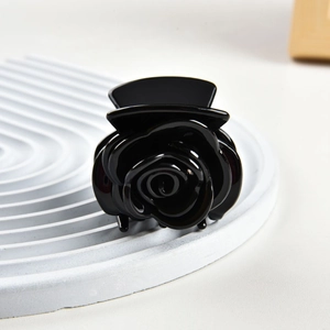 Close-up of a 3D black rose hair claw clip made of glossy resin on a decorative tray