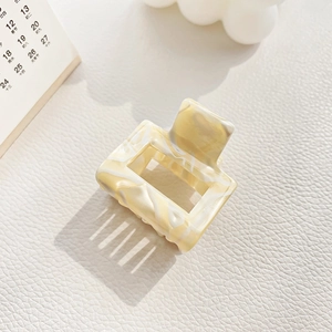 Detail view of a cream marble acetate hair claw clip on a textured white surface
