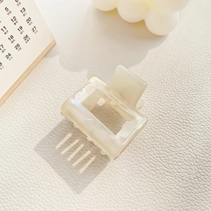 Detail of a square pearl acetate hair claw clip with a hollow design on white leather