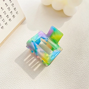 Detail of small square hair claw clip featuring rainbow tie-dye pattern on leather background